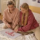 A mother and teenage daughter discuss reproductive health education while sitting on a bed with a schematic diagram.