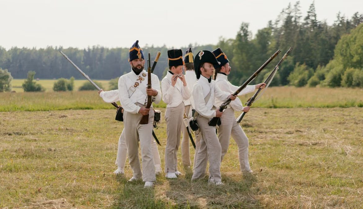 A group of men in historical military uniforms reenact a scene outdoors.