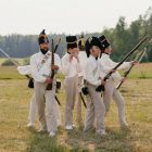 A group of men in historical military uniforms reenact a scene outdoors.