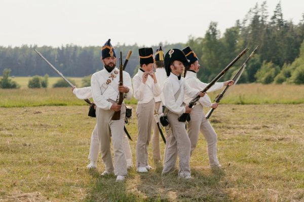 A group of men in historical military uniforms reenact a scene outdoors.