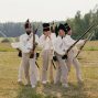 A group of men in historical military uniforms reenact a scene outdoors.