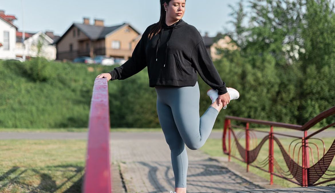 Young woman in activewear stretching on a red railing outdoors.